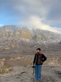 a woman standing on top of a dirt field next to a snow covered mountainside