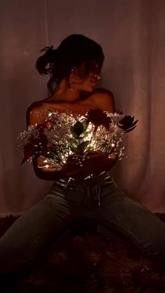 a woman sitting on the floor with flowers in her hands and lights behind her back