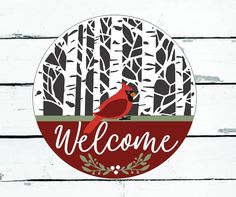 a red bird sitting on top of a welcome sign in front of a tree filled forest