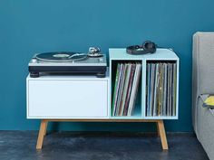 a record player sitting on top of a white cabinet next to a gray couch and blue wall