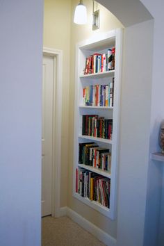 a white book shelf filled with books next to a wall mounted light above a doorway