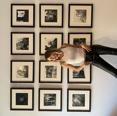 a woman is standing in front of many framed pictures on the wall with her hands on her hips