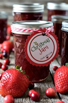 jars filled with jam sitting on top of a table next to strawberries and cranberries