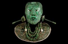 a green mask with beads on it's neck and two arrows sticking out of its mouth