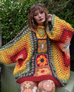 a woman wearing colorful crocheted clothing sitting on a bench