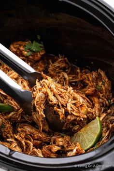 shredded meat in the crock pot with tongs and lime wedges on top