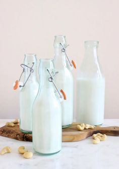 four glass milk bottles sitting next to each other on a wooden board with cashews