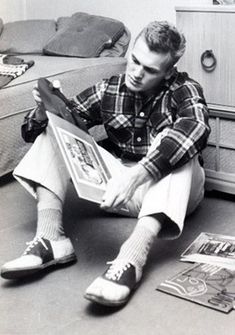 a young man sitting on the floor reading a book with his feet propped up in front of him