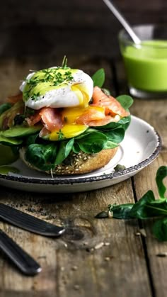 an open face sandwich with eggs, salmon and spinach on a plate next to a green smoothie