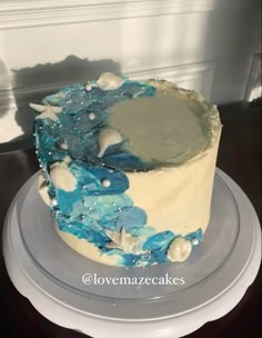 a blue and white cake sitting on top of a plate with seashells around it