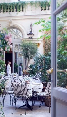 an outdoor dining area with tables, chairs and potted plants in the foreground