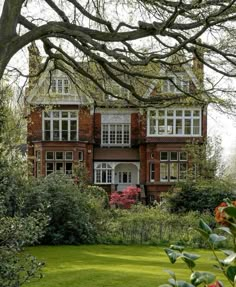 a large red brick house surrounded by trees and bushes with lots of windows on the top floor