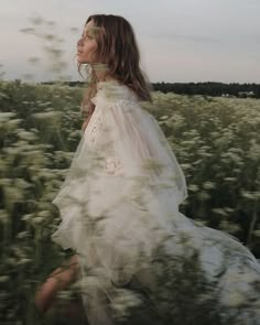 a woman in a white dress walking through a field