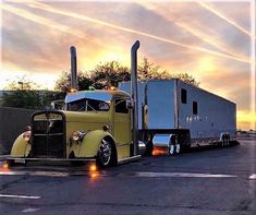 a yellow semi truck parked in a parking lot with the sun going down behind it