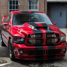 a red and black striped dodge truck parked in front of a brick building on the street