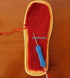 a crocheted red shoe with a blue needle in the middle on a wooden surface