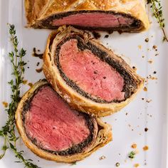 some meat is cut in half on a white plate with sprigs of herbs