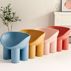 three different colored stools next to a potted plant in a room with white walls