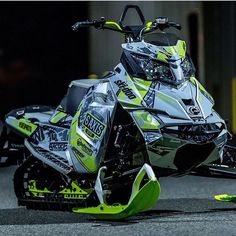 a green and black snowmobile sitting on the ground next to a yellow object in front of it