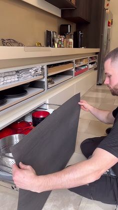 a man sitting on the floor looking at items in an open drawer with shelves behind him