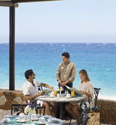 three people sitting at an outdoor table near the ocean