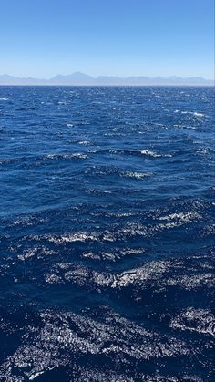 the water is very blue and there are some mountains in the distance on the horizon