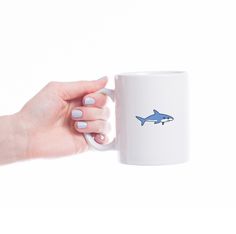 a woman holding a coffee mug with a shark drawn on it's side and the bottom half of her hand