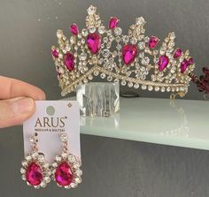 a pair of pink and white earrings with crystal drops on them, sitting next to a tiara