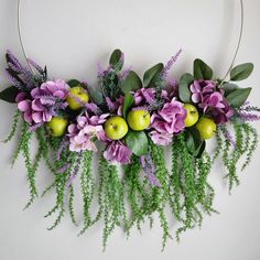 an arrangement of flowers and apples hanging on a wall with greenery in the middle