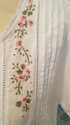 a white dress with pink flowers and green leaves embroidered on the front, sitting on a mannequin