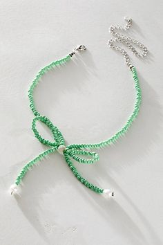 a green string bracelet with white beads and silver chains on a white surface, next to a chain