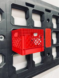 a red shopping basket hanging on the side of a black and white wall with holes in it