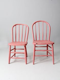 two pink chairs sitting next to each other on a white surface in front of a gray wall