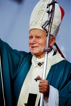 an older man in a priest's outfit waves to the crowd from behind him