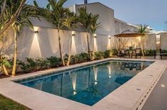 an outdoor swimming pool surrounded by palm trees and lights at dusk with patio furniture in the background