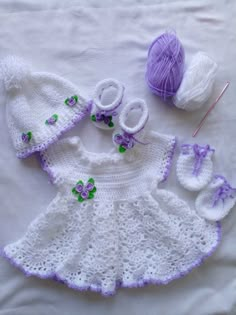 a crocheted baby outfit and booties are laying on a bed next to balls of yarn