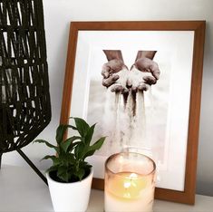 a framed photograph next to a potted plant and candle on a white table top