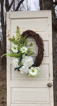 a wreath with white flowers hanging on the side of a door in front of a tree