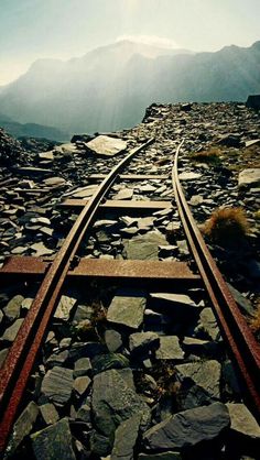 a train track going through the mountains with rocks and grass on each side in front of it