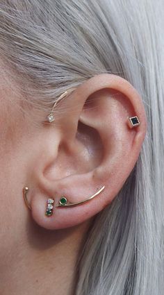 a woman with grey hair wearing an ear cuff and green stone piercings on her ears