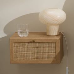 a white vase sitting on top of a wooden cabinet next to a glass filled with water