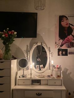 a white dresser topped with a mirror next to a vase filled with flowers and candles