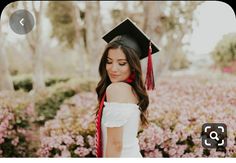 a woman wearing a graduation cap and gown standing in front of pink flowers with red tassels