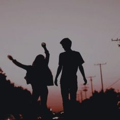 two people are walking in the dark with their arms up and one person is holding an object