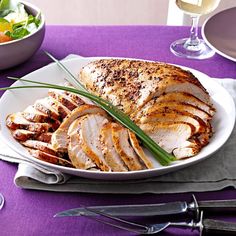 a white plate topped with sliced turkey next to a bowl of salad and wine glasses