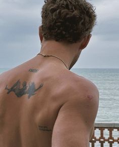 a man with tattoos on his back looking at the ocean