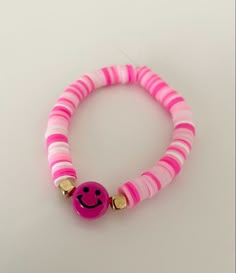 a pink and white bracelet with a smiley face beaded on it's end