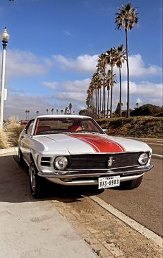 an old car is parked on the side of the road near palm trees and a street light