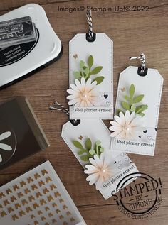 three tags with flowers on them are sitting next to some paper and stamping supplies