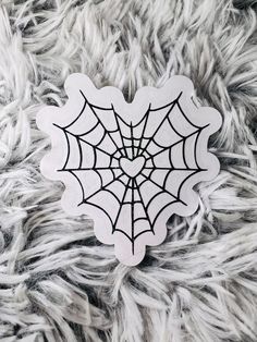 a spider web sticker sitting on top of a white furry surface with black outline